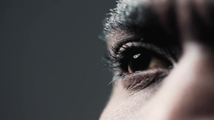 非裔美国人的眼睛在特写镜头中侧视。眼睑下有睫毛的虹膜和聚焦瞳孔的微距变焦图像。室内抽象黑人的角膜和视
