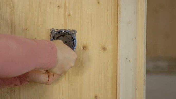 特写: 面目全非的女人在木墙上安装了一个电插座。