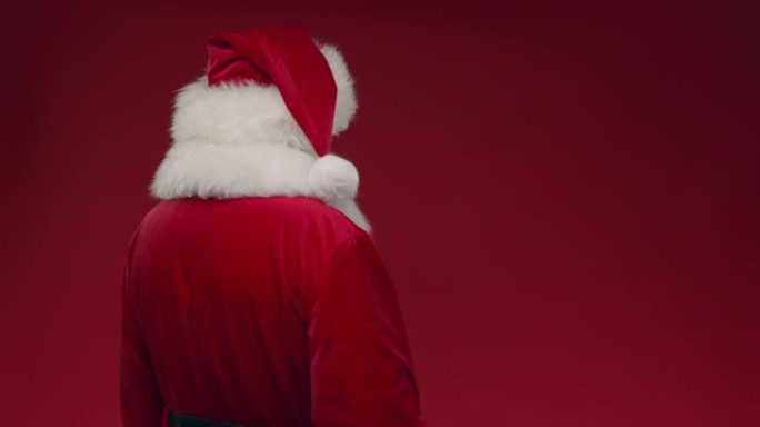 一个转身的圣诞老人在红色背景上向相机挥手，右边是复制空间