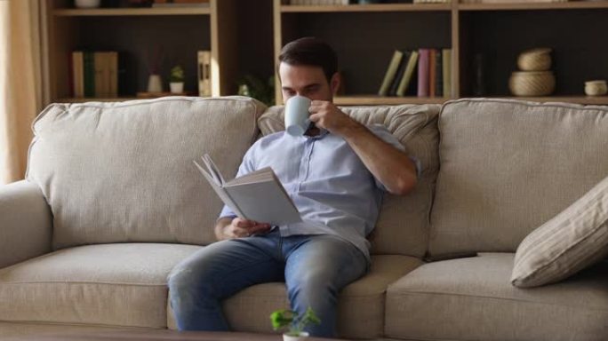 宁静的年轻男性坐在沙发上看书喝茶