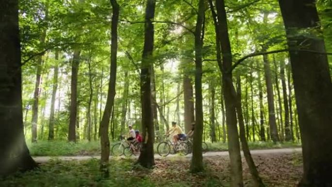 有三个孩子的SLO MO家庭在穿过森林的道路上骑自行车