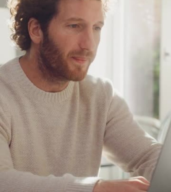 垂直屏幕: 成年男子，姜黄色卷发，使用笔记本电脑，坐在公寓的客厅。快乐的人在家工作，网上购物，看视频