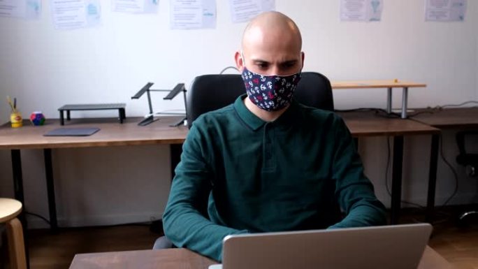 带有口罩的商人在办公室的笔记本电脑上工作