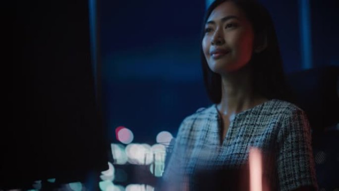美丽的亚洲女性肖像在黑暗现代办公室的台式电脑上工作。女商人晚上很晚在家工作。成年女性使用社交媒体，键