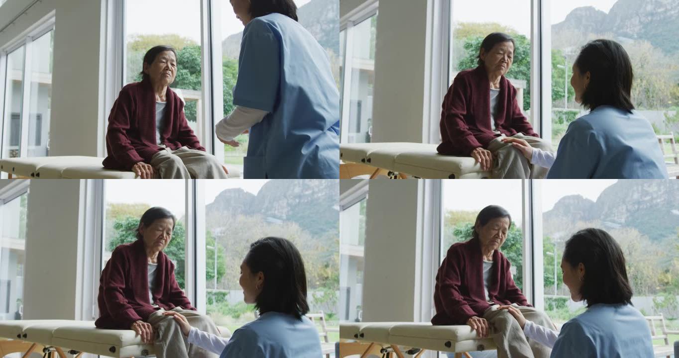 微笑的亚洲女性理疗师治疗高级女性患者的膝盖并在手术中交谈