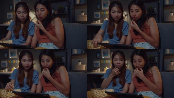迷人的亚洲女士与休闲享受快乐时刻焦点在平板电脑上观看在线电影娱乐晚上在家沙发客厅吃爆米花网站。生活方