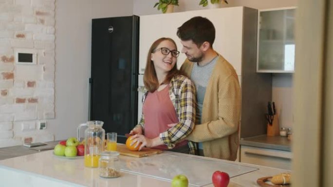 怀孕的女孩在厨房做饭和喂养丈夫，而男人抱着肚子，婴儿微笑