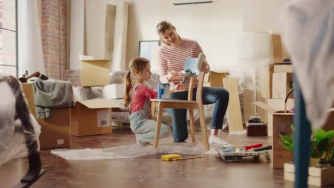 入住和家庭装修: 快乐的母女绘画复古家具椅，为新的舒适的家。开朗的年轻家庭使公寓充满艺术，色彩。微笑
