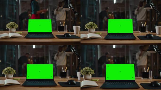 在繁忙的创意办公环境中，在桌子上放大带有绿屏模拟显示的笔记本电脑的镜头。任何媒体类型的隔离模板。真正