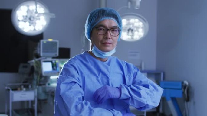 亚洲男外科医生戴着低面罩，在手术室交叉双臂的肖像