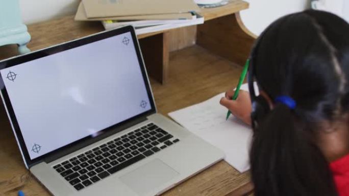 在线学校课堂上的混血女孩在家，使用屏幕上带有复印空间的耳机和笔记本电脑