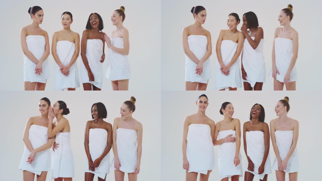 慢动作美丽的年轻女性的不同种族与完美的公司和苗条的身体在白色浴巾看和微笑在相机孤立的白色背景。