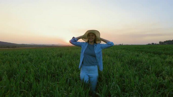 慢动作特写看日落时一名戴着草帽的美丽年轻女子在麦田里奔跑跳跃