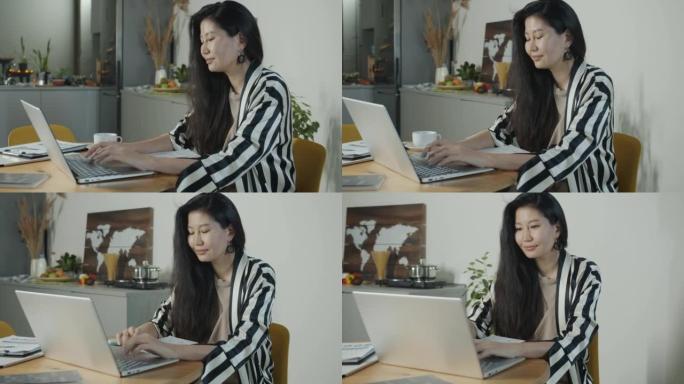 亚洲女性自由职业者在厨房桌子上用笔记本电脑打字在家在线工作的肖像