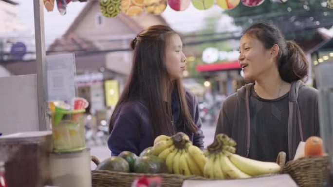 亚洲女友在摊位上选择水果做冰沙。泰国街头美食。