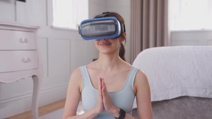 戴着虚拟现实耳机的女人坐在卧室的瑜伽垫上参加虚拟课堂