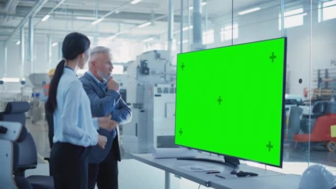 工厂办公室会议: 总工程师在带有绿屏模拟显示的电视的会议室中与业务合作伙伴交谈。重工业和制造业相关模