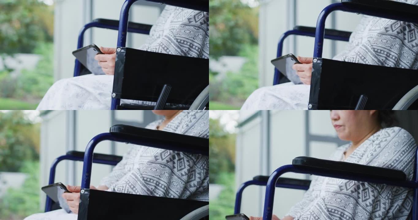 在医院使用智能手机坐在轮椅上的无聊的亚洲女性患者