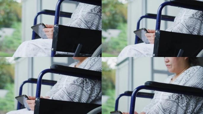 在医院使用智能手机坐在轮椅上的无聊的亚洲女性患者