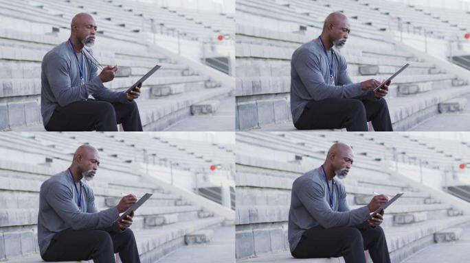 非裔美国男教练坐着，检查时间并做笔记