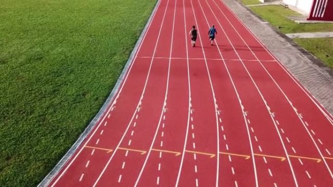 无人机正上方的运动观点亚洲华裔父子排队起跑线，在跑道上奔跑，并在早晨在看台旁的田径体育场奔向终点线