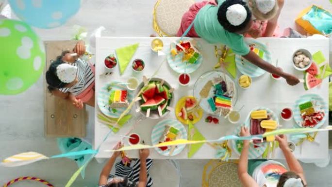 生日聚会，气球和蛋糕正在享受，而孩子们则在上面彩虹装饰的桌子上一起庆祝。夏季水果和甜食，孩子们一起玩