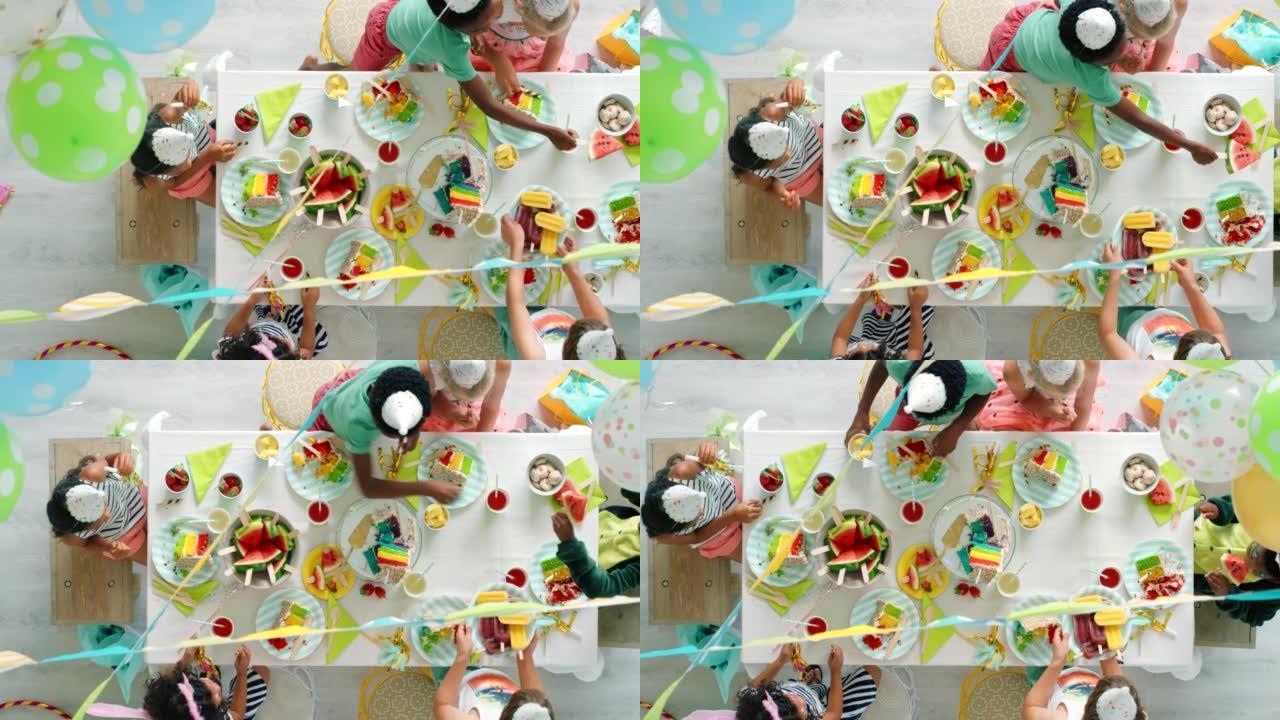 生日聚会，气球和蛋糕正在享受，而孩子们则在上面彩虹装饰的桌子上一起庆祝。夏季水果和甜食，孩子们一起玩