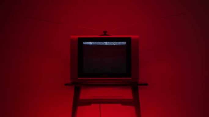 一台旧电视，在小桌子上的框架中间有电视静电噪音，在红色照明下