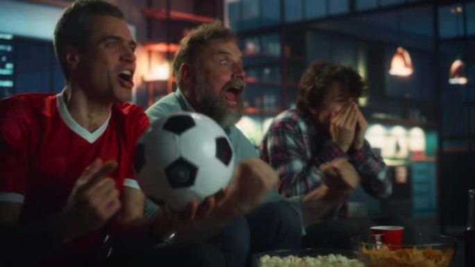 晚上在家: 三个快乐的足球迷坐在电视上的沙发上观看比赛，当运动队赢得冠军时庆祝胜利。当最喜欢的足球俱
