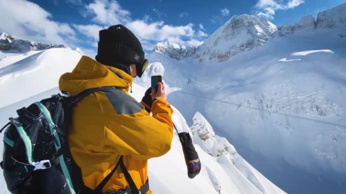 滑雪者在山脊顶上用智能手机拍照