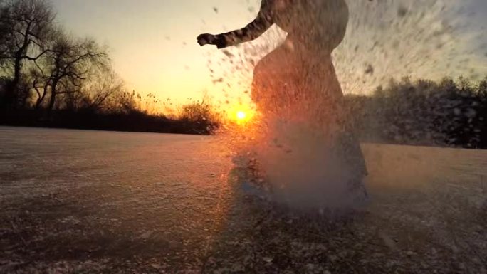 低角度: 男性滑冰运动员在日落时转向并向相机中喷射冰。