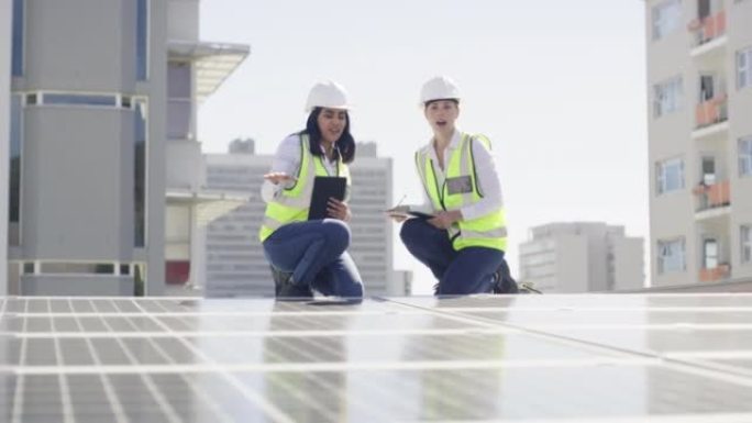 两个美丽的快乐自信的多民族年轻女工程师在安装太阳能电池板的建筑工地上工作时使用数字平板电脑并检查蓝图