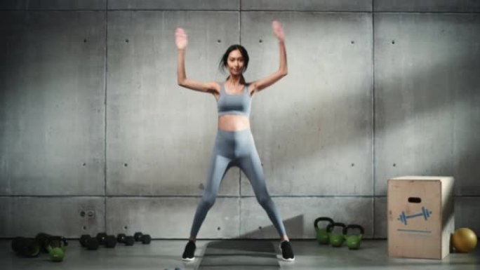 在线锻炼服务: 专业女性培训，锻炼。强壮的亚洲女人做跳跃千斤顶。时尚简约背景。慢动作电影宽肖像