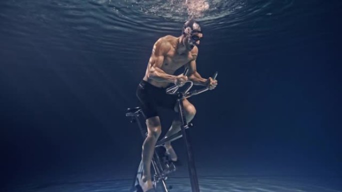 年轻的男性运动员的电影镜头肌肉发达，正在水下固定的骑行机上努力和决心地运动。运动、健身、健康生活方式