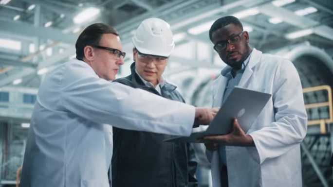 由各种专业的重工业工程师组成的团队，他们穿着安全制服和安全帽在笔记本电脑上工作。技术人员和工人在工厂