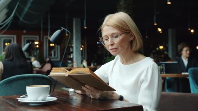 聪明的商务女士成熟的金发阅读书在餐厅放松