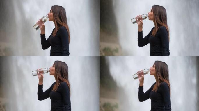 年轻女子在瀑布前喝水