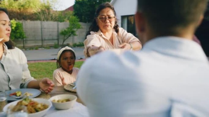 多代家庭在后院的一张桌子上共享一顿饭。亚洲孩子、祖父母和父母在家里的户外用餐区庆祝节日和吃午餐
