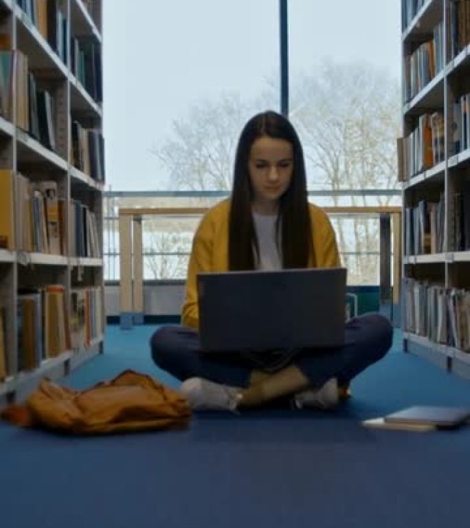 SLO MO年轻女学生在图书馆书架之间的笔记本电脑上工作