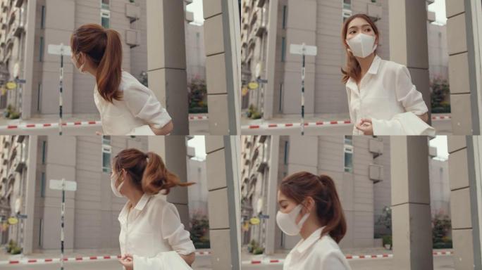 穿着时尚办公服装的成功年轻亚洲女商人戴着医用口罩，独自在城市现代城户外行走。