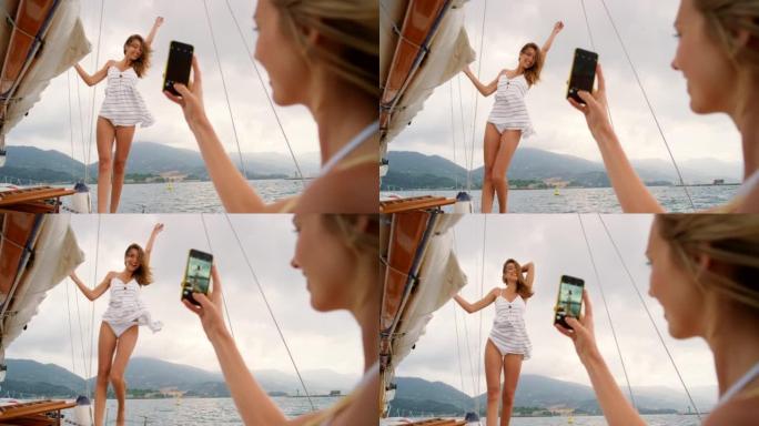 无忧无虑的快乐年轻女子在游艇上与朋友在智能手机上拍照。年轻女子在游艇上的假日巡游中用手机给朋友拍照