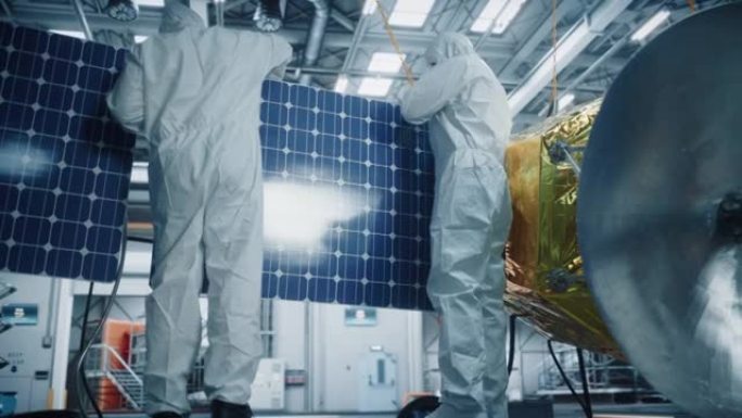 从事卫星施工防护服的工程师和技术人员。航空航天局: 科学家团队将太阳能电池板的机翼固定在航天器上。国