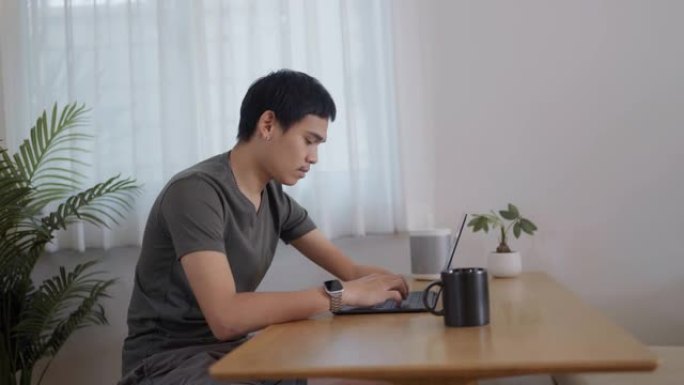 一个年轻人用笔记本电脑和咖啡在室内工作，家庭办公室的概念。
