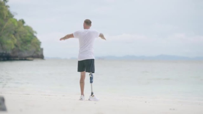 早上在海滩上做伸展运动的假肢残疾男子的后视图。残疾收藏: 日常生活理念