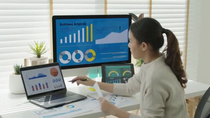 年轻迷人的亚洲泰国女性员工忙于在线工作多屏幕笔记本电脑或智能平板电脑在家自由销售数据分析，数据科学科