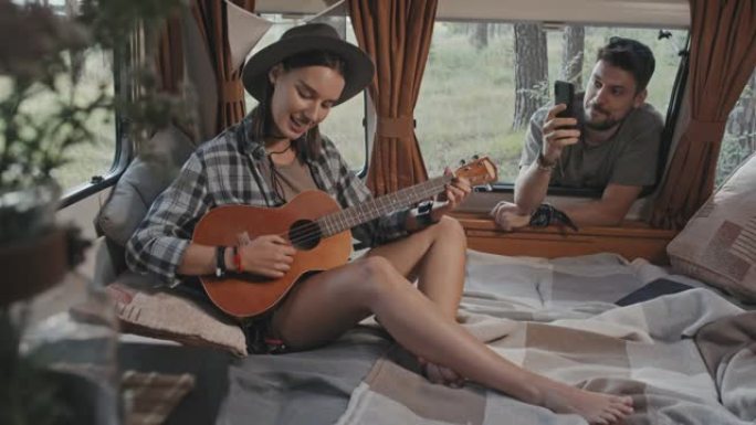 男子在露营车中拍摄女子演奏夏威夷四弦琴