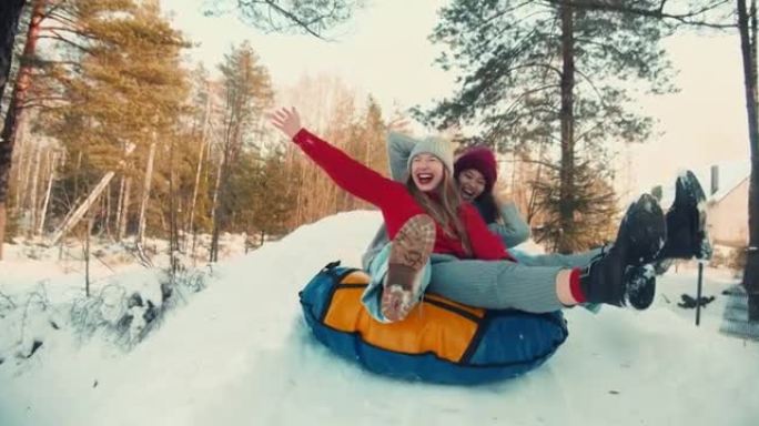 两个多民族兴奋快乐美丽的朋友女人微笑雪橇在雪坡上对着镜头，冬天有趣的慢动作。