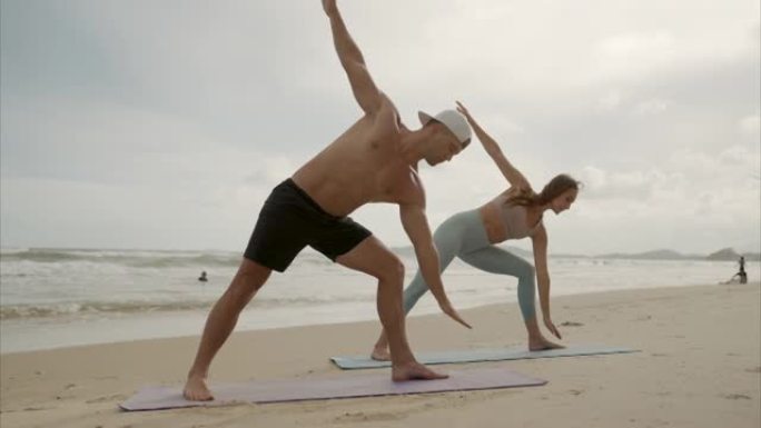 运动女人和男人在海滩上做瑜伽