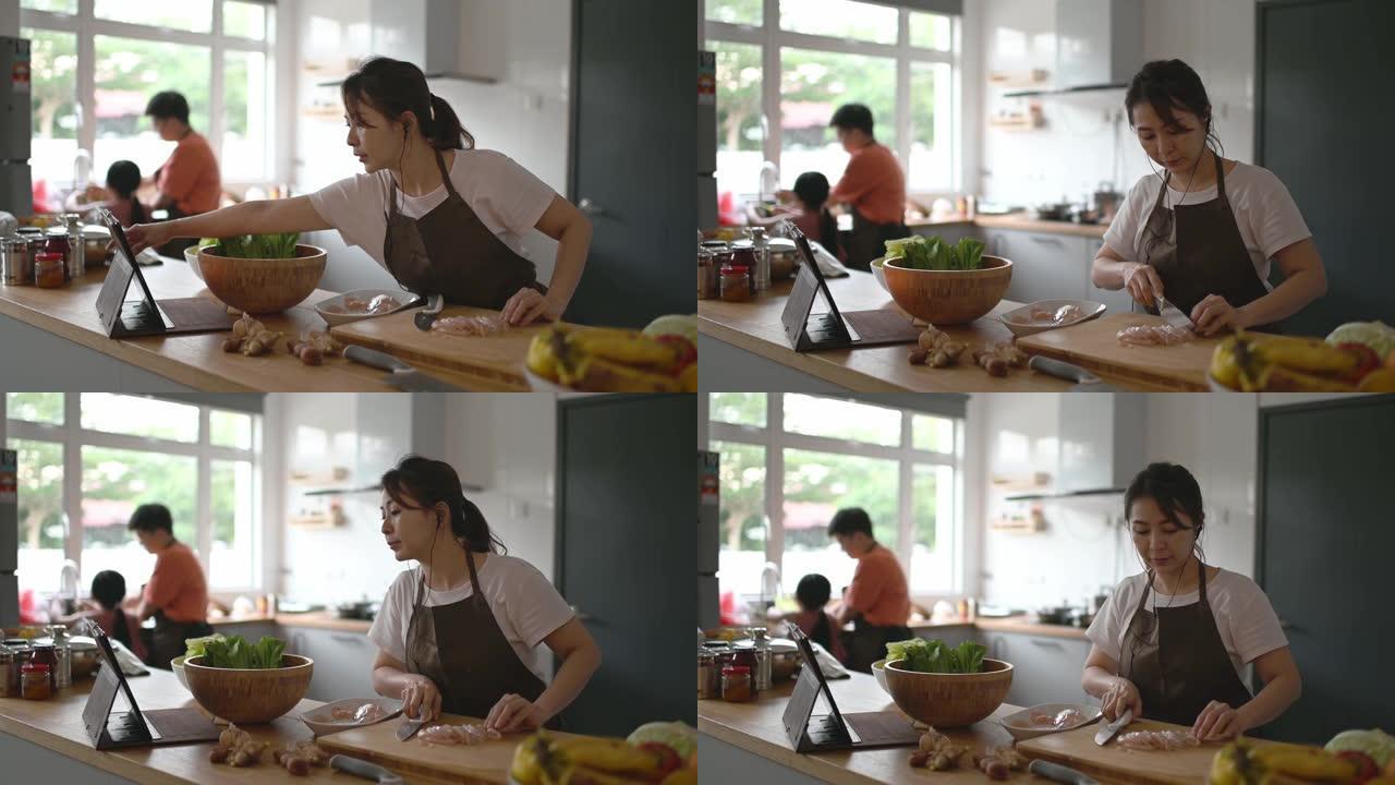 亚洲华人母亲在厨房柜台做饭，并使用数字平板电脑从互联网上学习食物