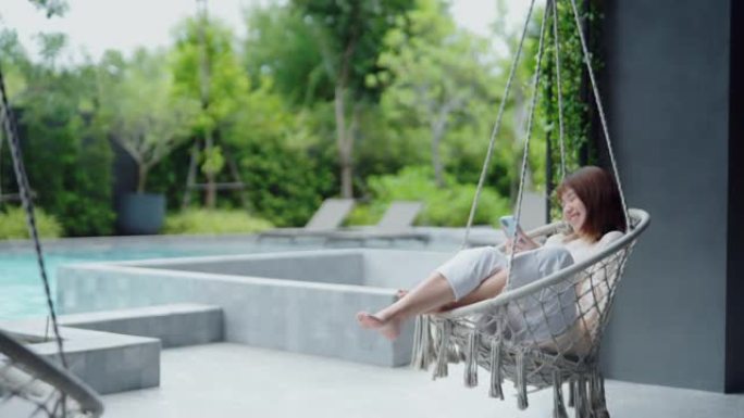 女人在室外酒店游泳池旁的吊床秋千上放松。